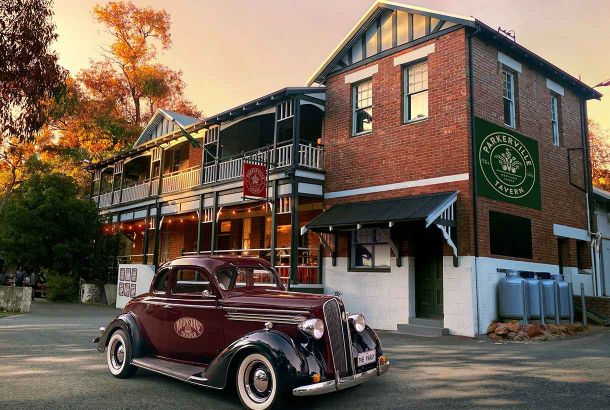 Parkerville Tavern heritage listed two storey federation style pub with wrap around veranda, warm evening glow and a 1936 Plymouth Business Coupe parked out the front